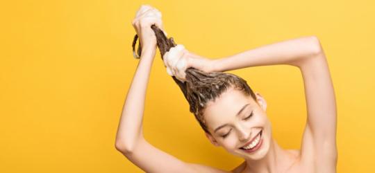 Żółte tło, kobieta owinięta ręcznikiem myje włosy.